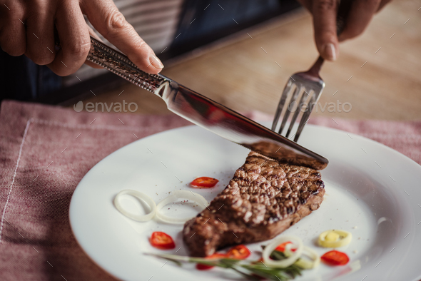 Close up partial view of woman eating steak with fork and knife