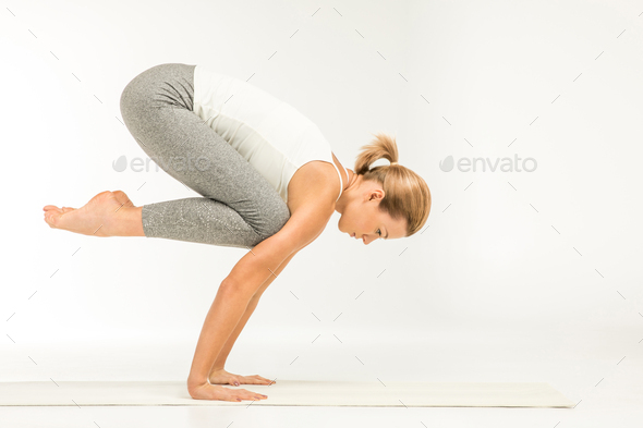 Young Attractive Woman Practicing Yoga, Standing In Bakasana Exercise, Crane  Pose, Working Out Wearing Sportswear, Top And Pants, Indoor Full Length,  White Loft Studio Background Stock Photo, Picture and Royalty Free Image.