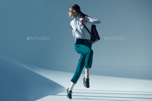 young stylish hipster woman in white shirt, green trousers and glasses looking away while jumping
