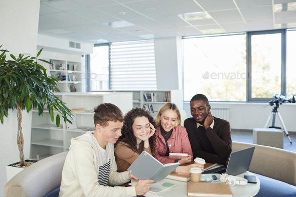 Multi-ethnic group of cheerful young people studying together while sitting at table in college library and working on group project, copy space