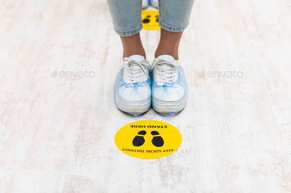 Female Feet Standing Near Social Distancing Warning Sign On Floor