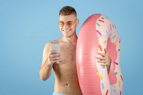 Online tourist agency. Young man with inflatable ring and smartphone booking tropical tour on web