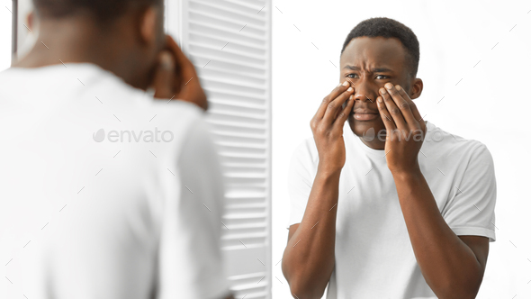 Concerned African Man Touching Bags Under Eyes Standing In Bathroom