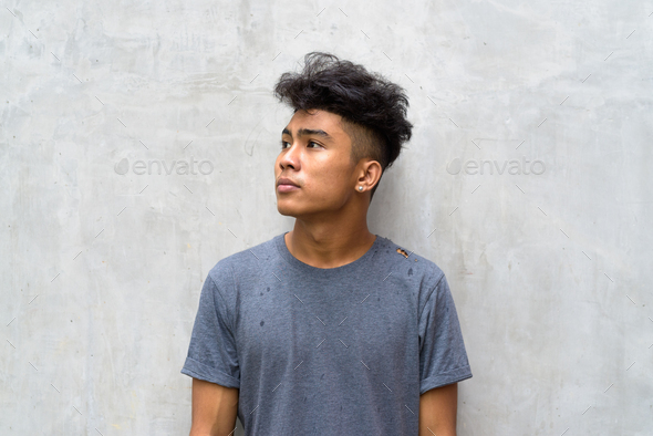 Young Asian Man With Curly Hair Thinking Against Concrete Wall Outdoors  Stock Photo By Amazingmikael