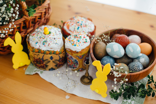 Homemade easter cake, stylish easter eggs natural dyed, candle, bunny decor, green branches and flowers on wooden background. Easter Food for sanctify. Happy holiday