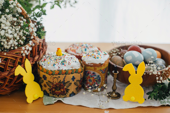 Homemade easter cake, stylish easter eggs natural dyed, candle, bunny decor, green branches and flowers on wooden background. Easter Food for sanctify. Happy holiday