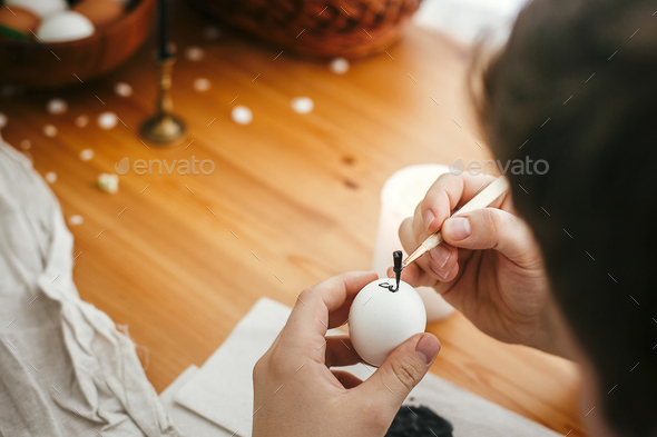 Hands painting easter egg with hot wax on background of wooden table. Modern Easter eggs with stylish wax ornaments. Happy Easter. Zero waste. Ukrainian traditional egg pysanka