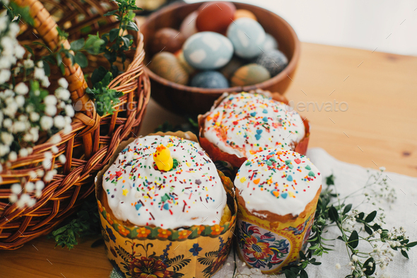 Traditional Easter food on rustic table. Homemade easter cake, easter eggs natural dyed, candle, green branches and flowers with wicker basket on wooden background. Easter Food for sanctify