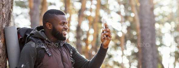 African man backpacker with smartphone in forest, happy to get connection, panorama with copy space