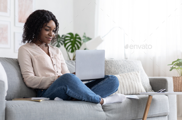 Online Education. Young Black Woman Studying With Laptop At Home, Sitting On Couch And Browsing Internet On Computer, Enjoying Distance Learning, Watching Webinar, Typing On Keyboard, Free Space