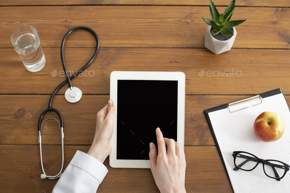 Modern private practice of doctor. Hands of female doctor works on tablet with blank screen on