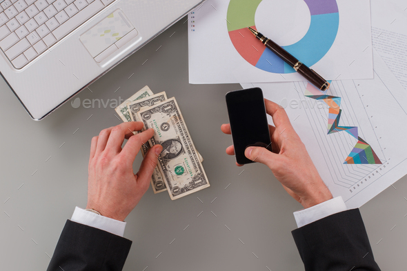 Male hands holding smartphone and money on office desk.