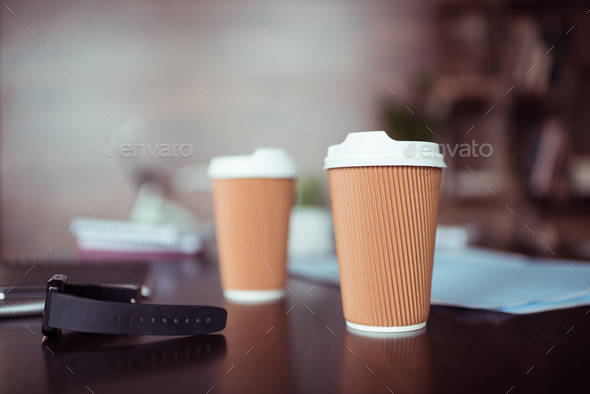 Close-up view of smartwatch and disposable coffee cups on table