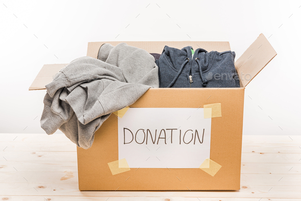 cardboard box with donation clothes on wooden table isolated on white, donation concept