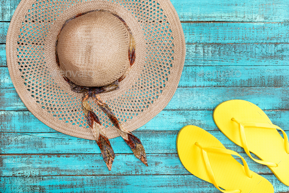 Top view of straw hat and yellow flip-flops on blue wooden table, summer concept