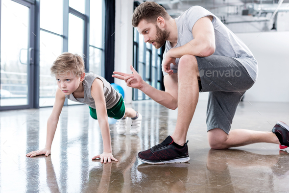Boy doing push ups with coach at fitness center