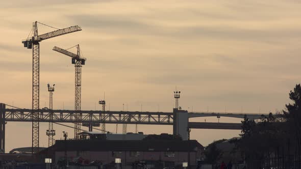 Construction cranes next to the 25Th Lisbon Bridge in the sunset. Suspension Bridge connecting the c alt