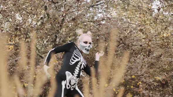 A girl with a scary make-up in a skeleton costume, in a mask with rhinestones in a gloomy autumn for alt