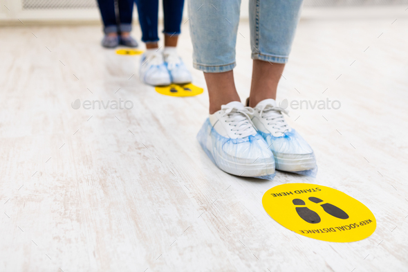 People Standing In Queue, Social Distancing Signs On Floor Indoors