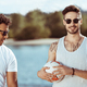 two multicultural friends in sunglasses holding volleyball ball on riverside - PhotoDune Item for Sale