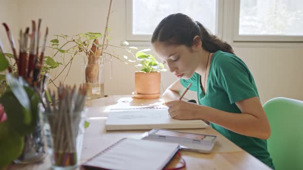 Teenage artist sitting drawing in a sketchbook in her room alt