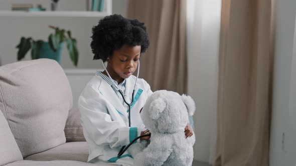Serious African American Kid Girl Sitting in Room on Couch in Medical Uniform Pretending to Be alt