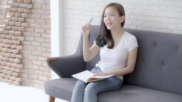 Beautiful young asian woman sitting on couch study and learning writing notebook at home. alt