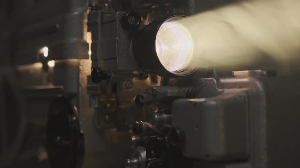 Old film projector projecting beam of light in dark room or movie theater alt