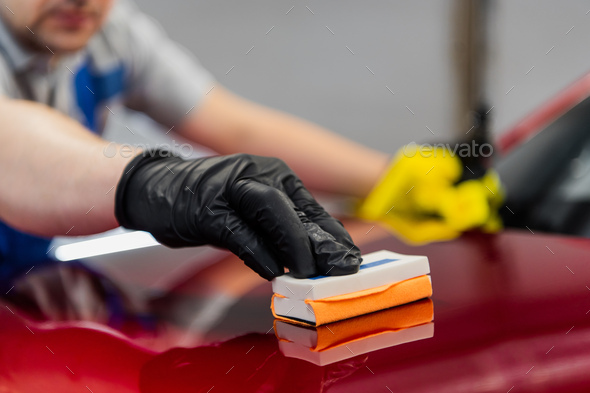 Man worker of car detailing studio applying ceramic coating on car paint with sponge applicator