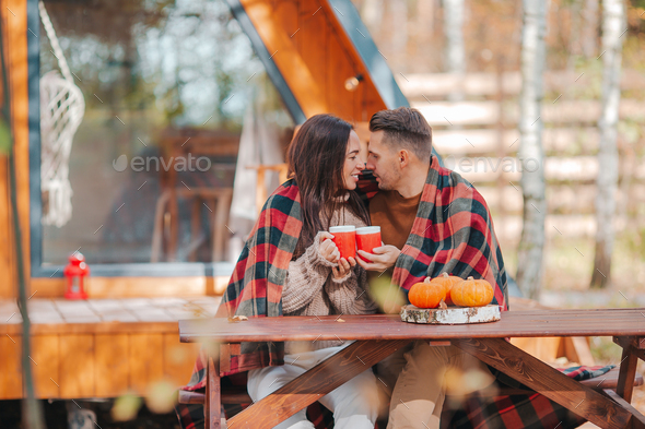 Young couple sitting on the wooden old table in the autumn forest background of their house