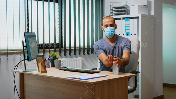 Man wearing mask and disinfecting hands in workplace before typing on keyboard. Entrepreneur cleaning using sanitize alcohol gel against corona virus, working in new normal office workplace in company