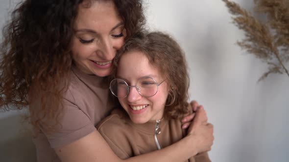 Happy Affectionate Young Mom Hugging Teen Daughter Looking at Camera Standing Home alt