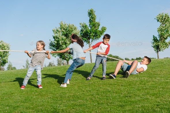 Cheerful multiethnic kids pulling rope and playing tug of war in park Stock  Photo by LightFieldStudios