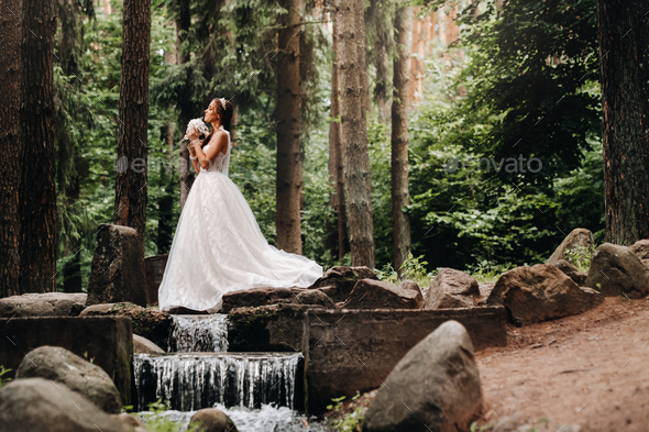An elegant bride in a white dress and gloves holding a bouquet stands ...