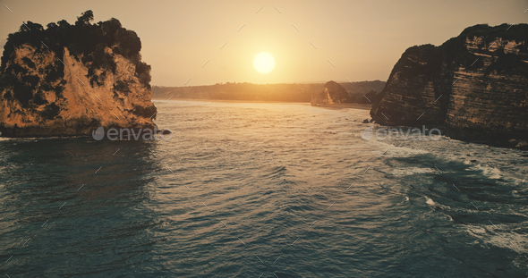 Sunset at rock ocean shore with waves at water surface in aerial view. Epic nobody nature at sun set