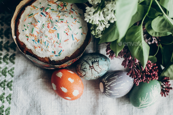 happy easter. easter cake and colorful decorated eggs on rustic background with lilac flowers. egg with floral and chicken ornaments. space for text. greeting card concept. top view