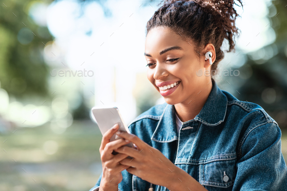 Happy Black Lady Using Smartphone Texting Sitting In Park Outdoor