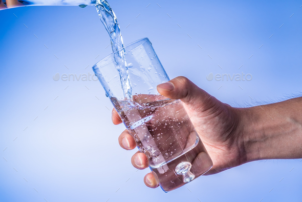 Filling up the glass with water, hand holding glass against bright blue  background Stock Photo by IciakPhotos