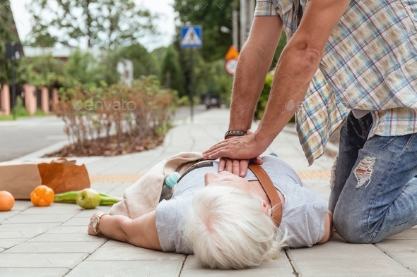 Man performs a heart massage on an senior lady who fainted on the street