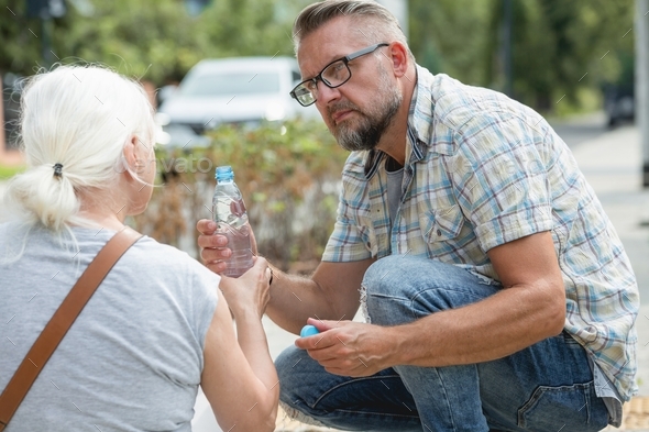 Middle age man gives a bottle of water to a woman who fainted on the street