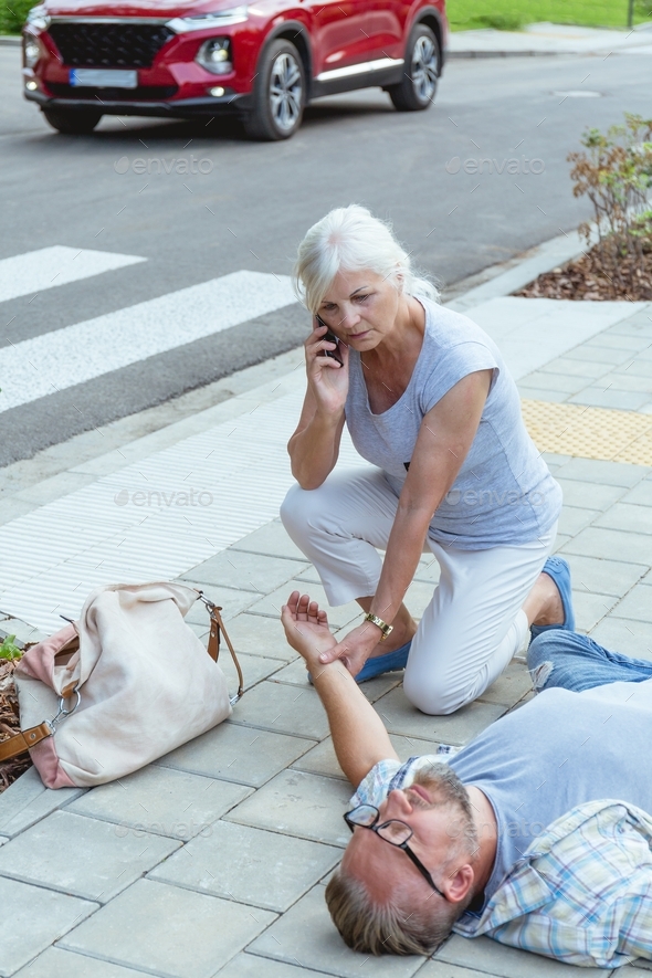 Senior passerby kneels beside the person who fainted on the street and calls an ambulance