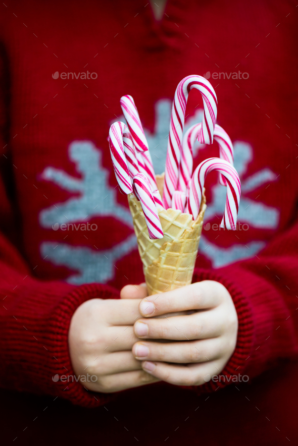 Little girl in a Red Xmas Jumper is holding Red Candy Canes in an Ice Cream Waffle Cone, Winter and Christmas time concept