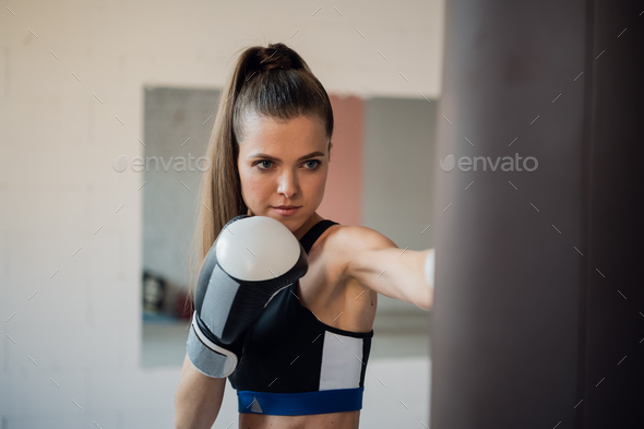 A girl in sports clothes is engaged in boxing and works out a punch with her hand on a punching bag.