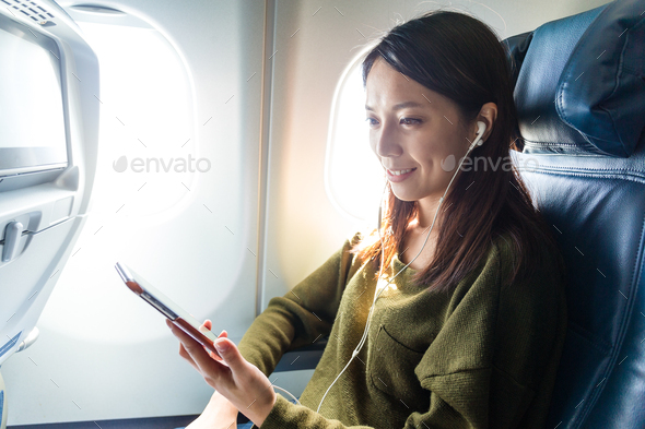 Woman passenger in airplane using cellphone with earphone