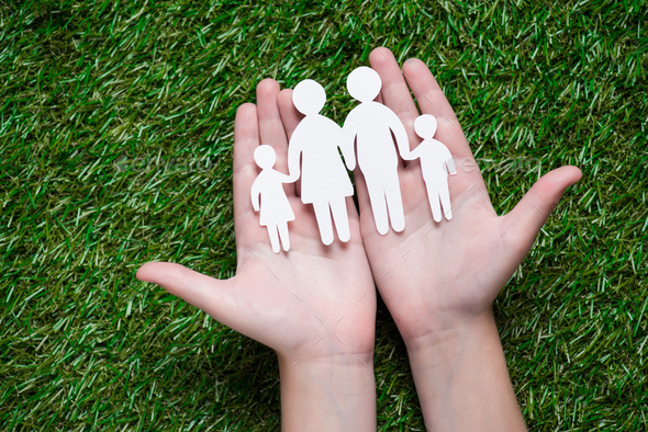 human hands holding paper cut of family on grass