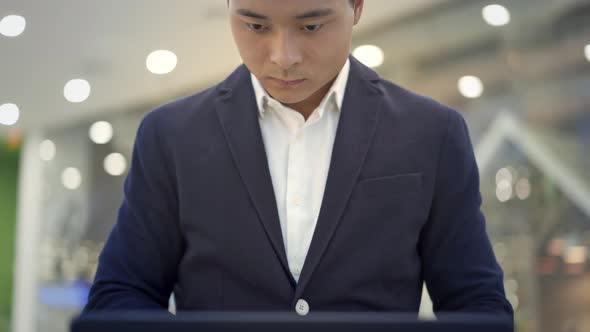 Tilt Up Shot of Asian Male Businessman in Suit Working with Laptop on His Knees