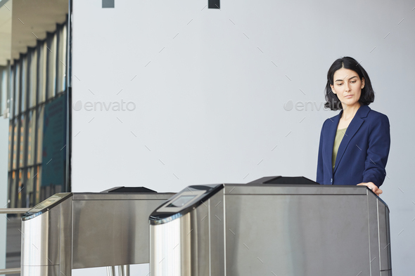 Portrait of contemporary Middle-Eastern businesswoman swiping card while passing turnstile gate in airport or office building, copy space