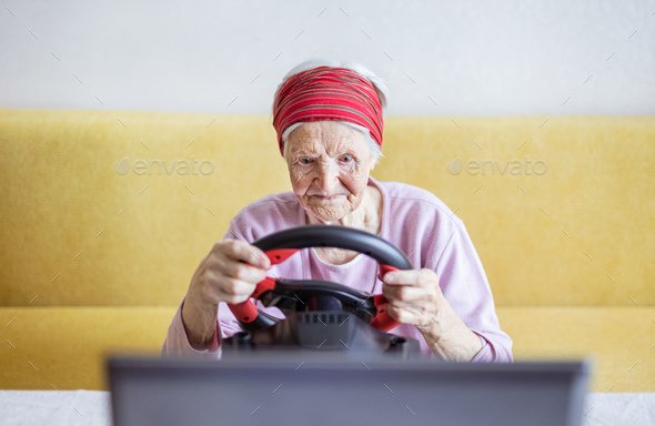 Senior woman enjoying car racing video game on laptop while sitting on couch - Stock Photo - Images
