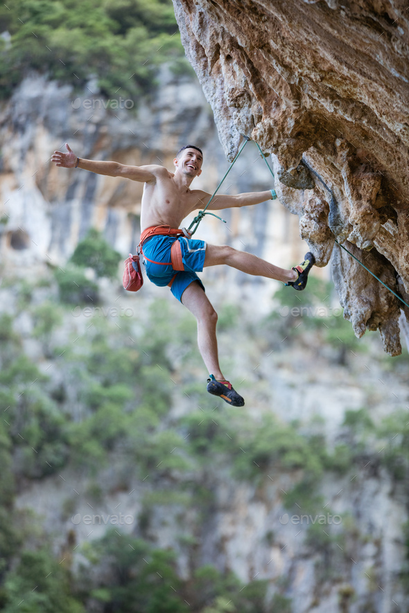Cheerful rock climber hanging on rope while climbing challenging route - Stock Photo - Images