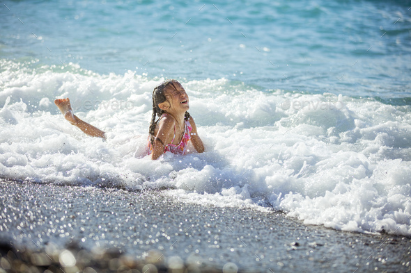 Happy young girl playing in waves on beach - Stock Photo - Images